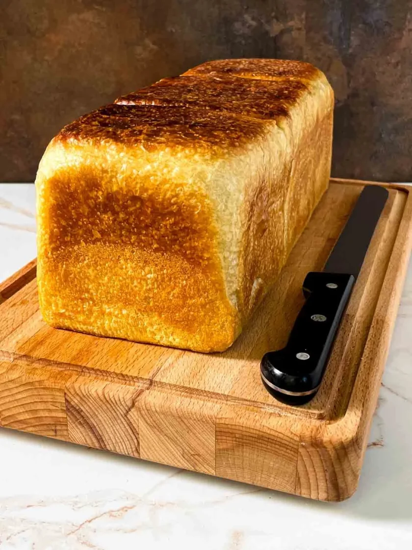 Una barra de pan y un cuchillo de sierra sobre una tabla de cortar de madera.