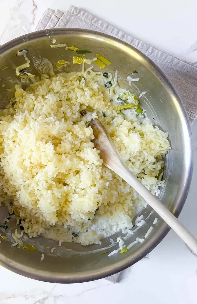 Una sartén profunda con puré de papas, en la misma sartén hay un poco de verduras y cuchara de madera.