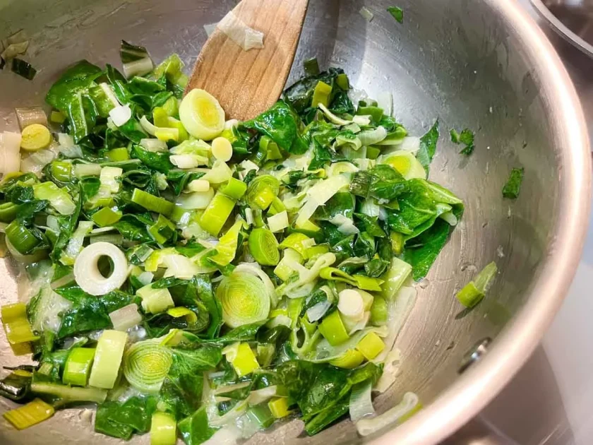 Puerros y verduras picados que se saltean en una sartén con una espátula de madera.
