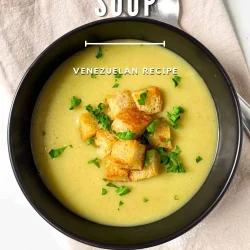 A bowl of creamy leek and potato soup topped with croutons and herbs, with a spoon beside it on a cloth napkin.