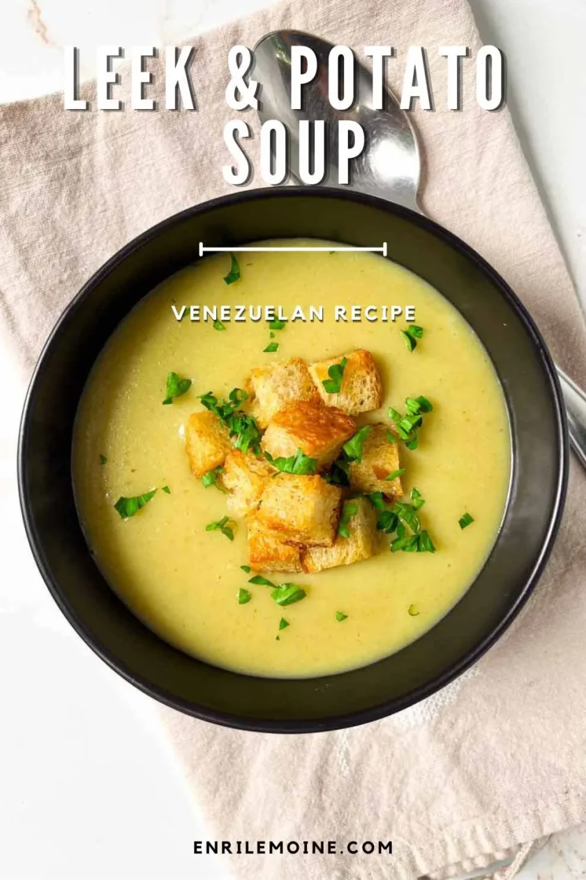 A bowl of creamy leek and potato soup topped with croutons and herbs, with a spoon beside it on a cloth napkin.