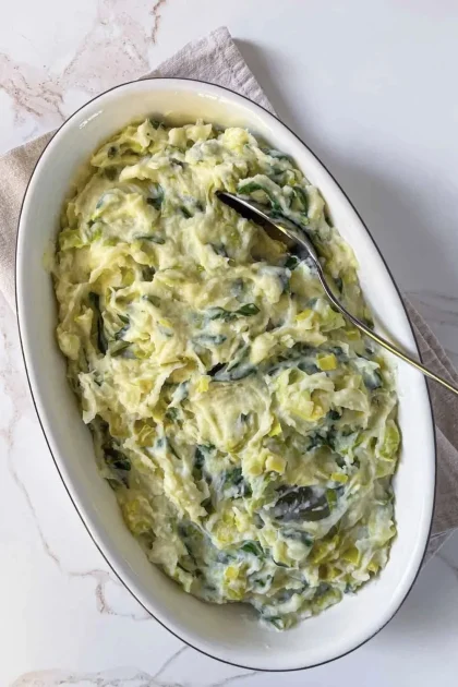Cremoso puré de papas con ajo porro y acelgas servido en un plato blanco ovalado, con una cuchara apoyada encima.
