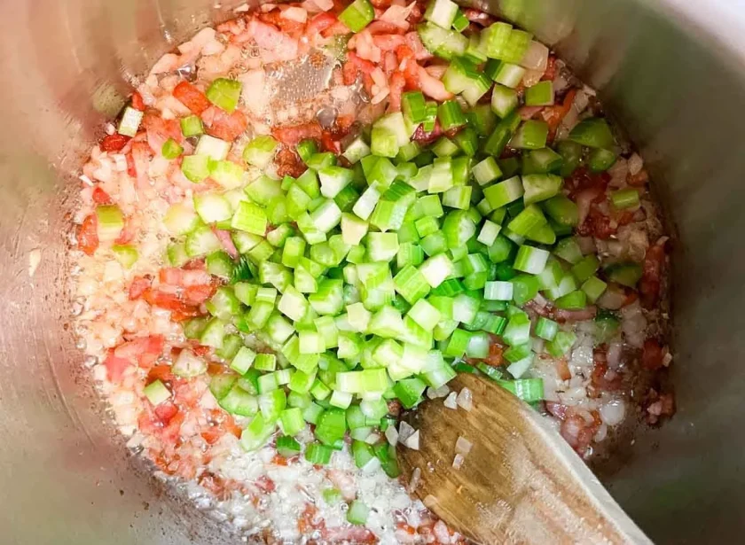 Una olla vista desde arriba con unsofrito que tiene tocineta, cebolla y apio.