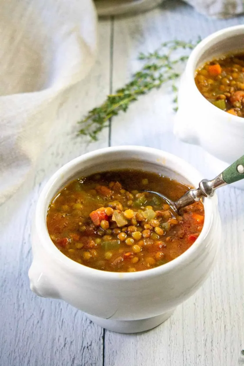 Dos cuencos de sopa de lentejas a la italiana con unas ramitas de tomillo an fondo, sobre una superficie de madera blanca.