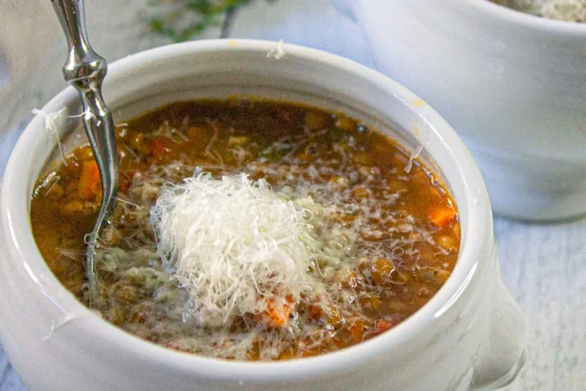 Un tazón de sopa de lentejas a la italiana con abundante queso parmesano rallado.