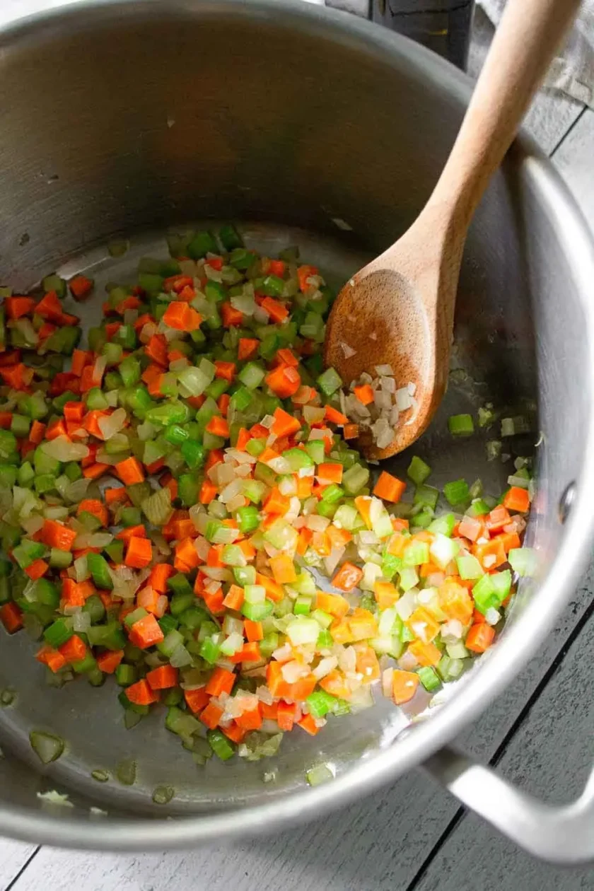 Se rehogan zanahorias, apio y cebollas en una olla con una cuchara de madera, para hacer la base una sopa de lentejas a la italiana.