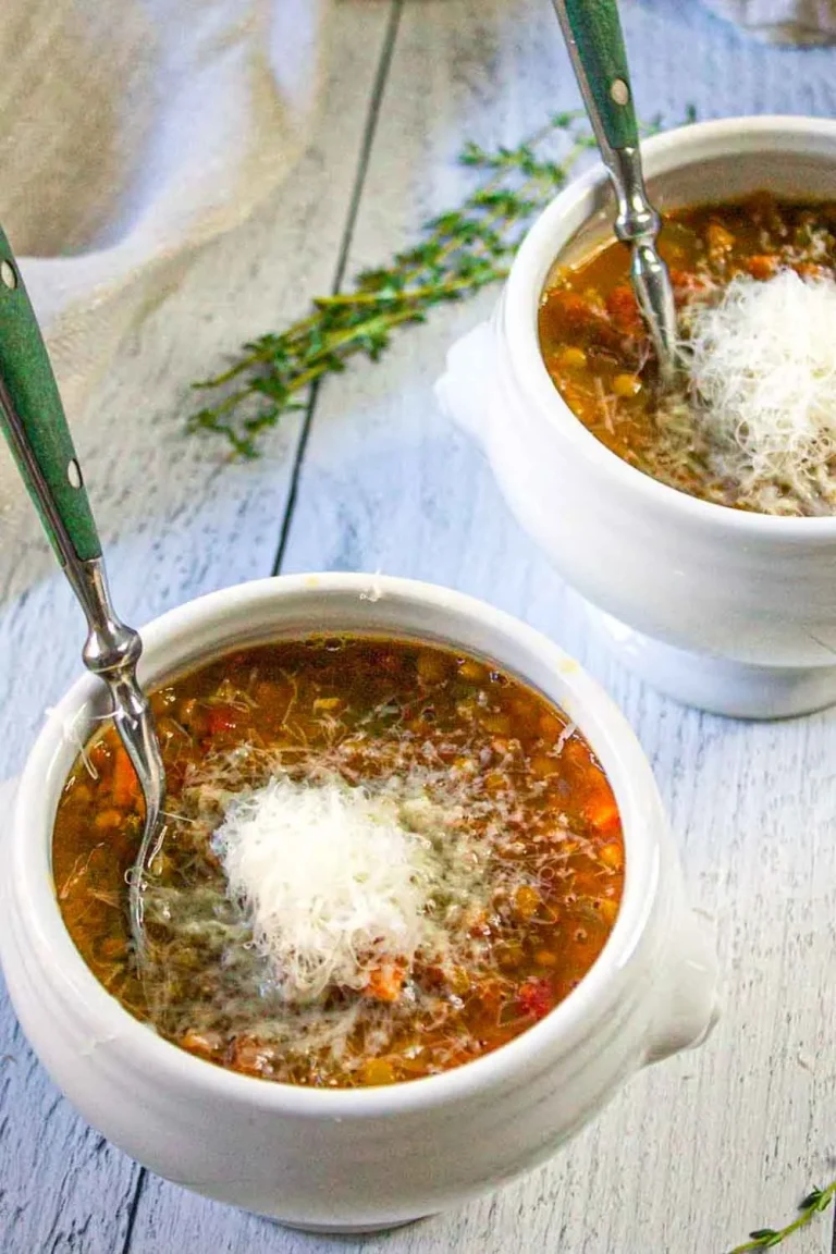 Two bowls of Italian-Style Lentil Soup are served with a fspoon, ready to enjoy with a sprinkle of Parmesan cheese.
