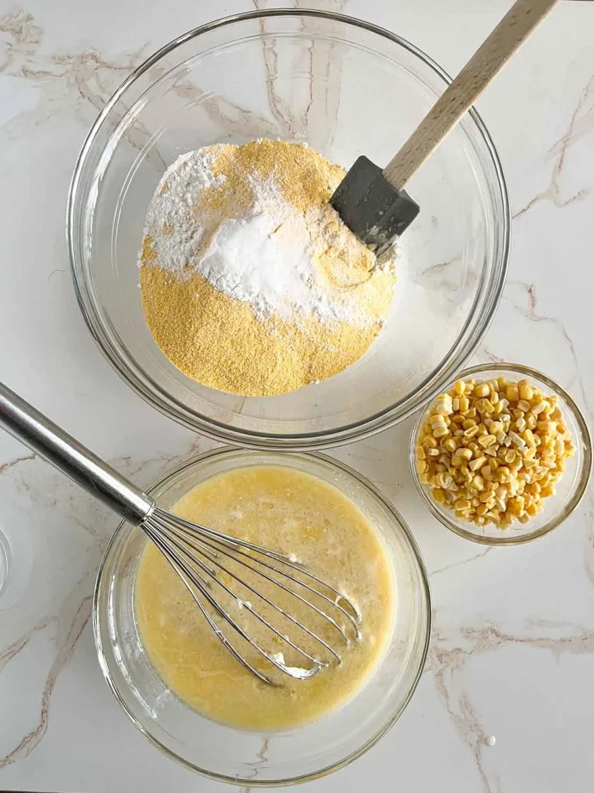 Tres cuencos con la mezcla de harina de maíz, los ingredientes húmedos batidos y los granos de maíz sobre una encimera de mármol.