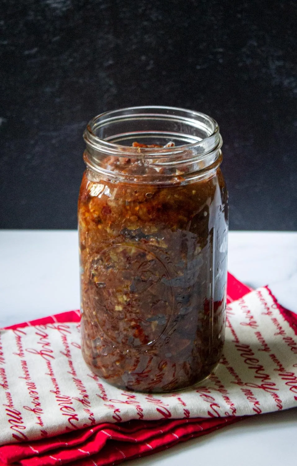 Un tarro de cristal lleno de macerado de macerado marrón para torta negra está colocado sobre una tela roja y blanca.