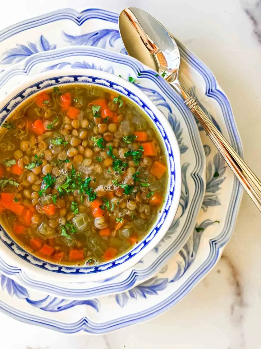Un cuenco de sopa de lentejas con tocineta con una cuchara y un plato.