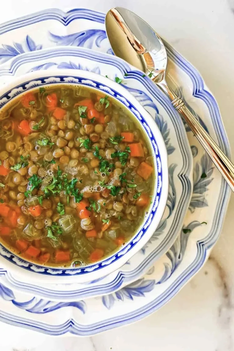 Bowl of French Bistro-Style Lentil Soup with Bacon, featuring chopped carrots and parsley on decorative blue and white plates, with a spoon beside. Try this classic dish—ready in just 40 minutes!.