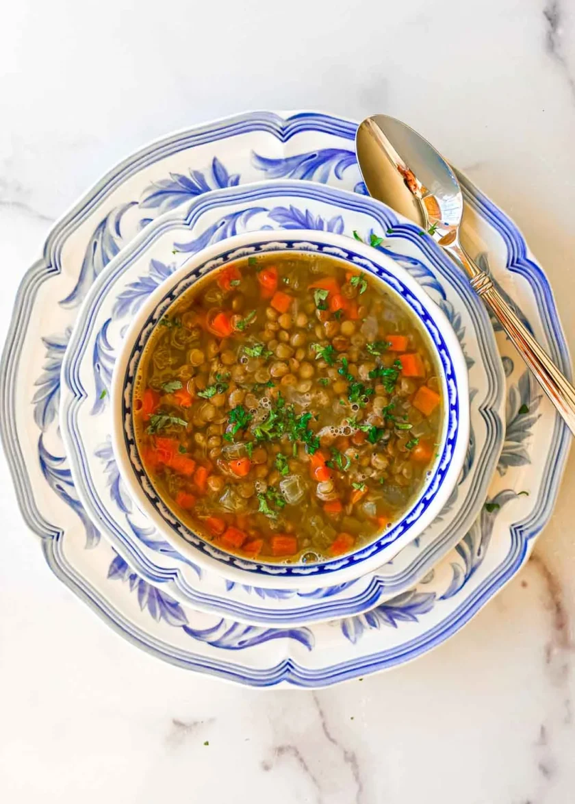 Bowl of lentil soup with carrots and herbs on decorative blue and white plates, with a spoon beside it.