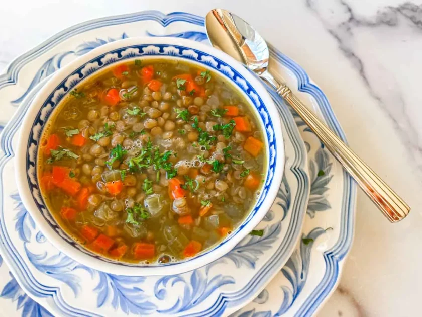 A bowl of lentil soup with carrots and herbs, served on blue and white patterned dishes with a spoon.