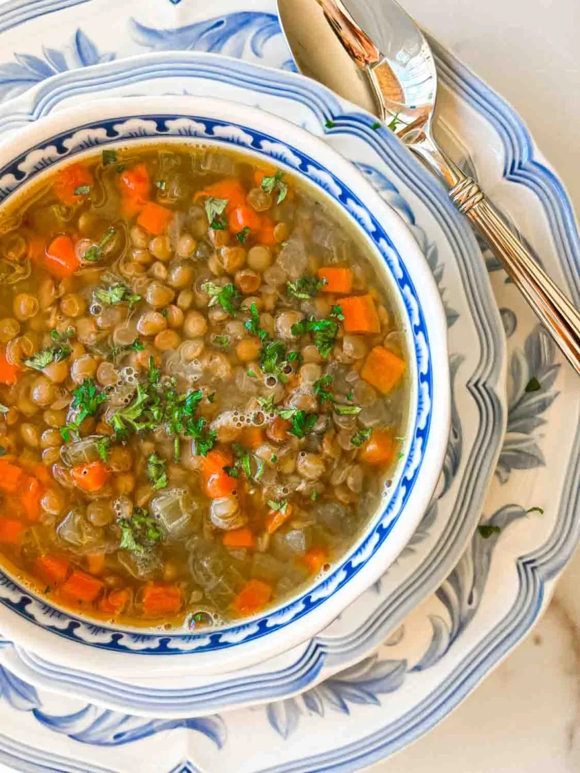 Un cuenco de sopa de lentejas con zanahorias y hierbas, servido en platos decorativos azules y blancos con una cuchara.