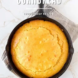Golden cornbread baked in a cast iron skillet, this easy cornbread rests on a gray cloth over a marble surface.