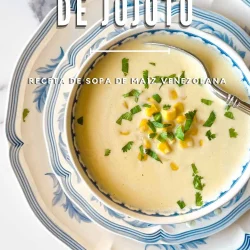 Tazón de sopa cremosa de maíz con guarnición de maíz y hierbas, servido en platos florales con cuchara.