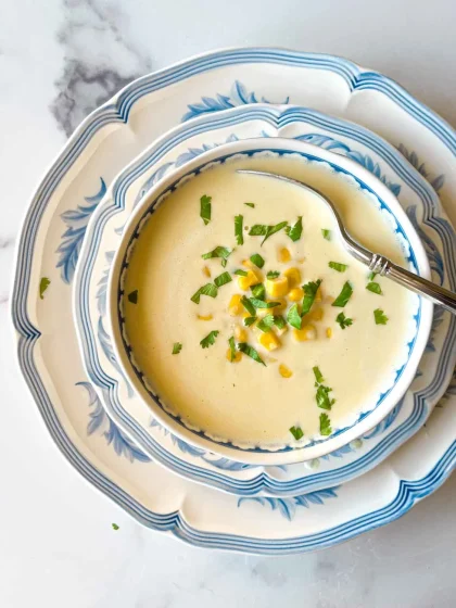 A bowl of creamy crema de jojoto topped with corn and chopped herbs, served on blue and white plates with a spoon.