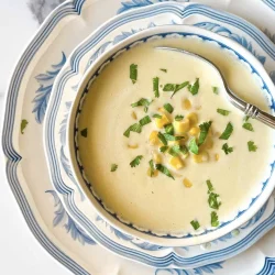 Un cuenco de sopa cremosa de maíz, o crema de jojoto, adornado con hierbas y servido en platos azules y blancos apilados con una cuchara.