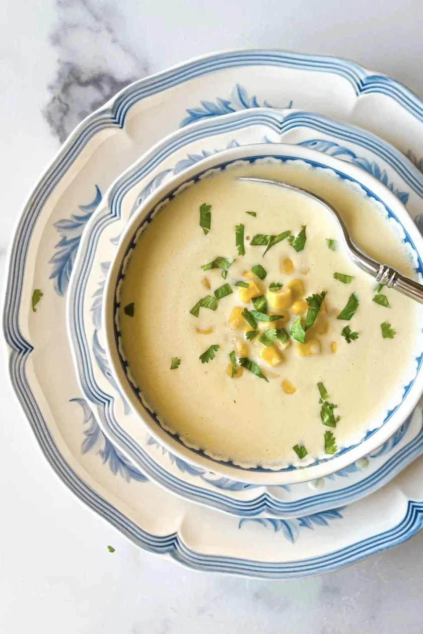 Un cuenco de cremosa crema de jojoto, una clásica receta venezolana con maíz y hierbas, servida en platos con motivos azules y blancos con una cuchara.