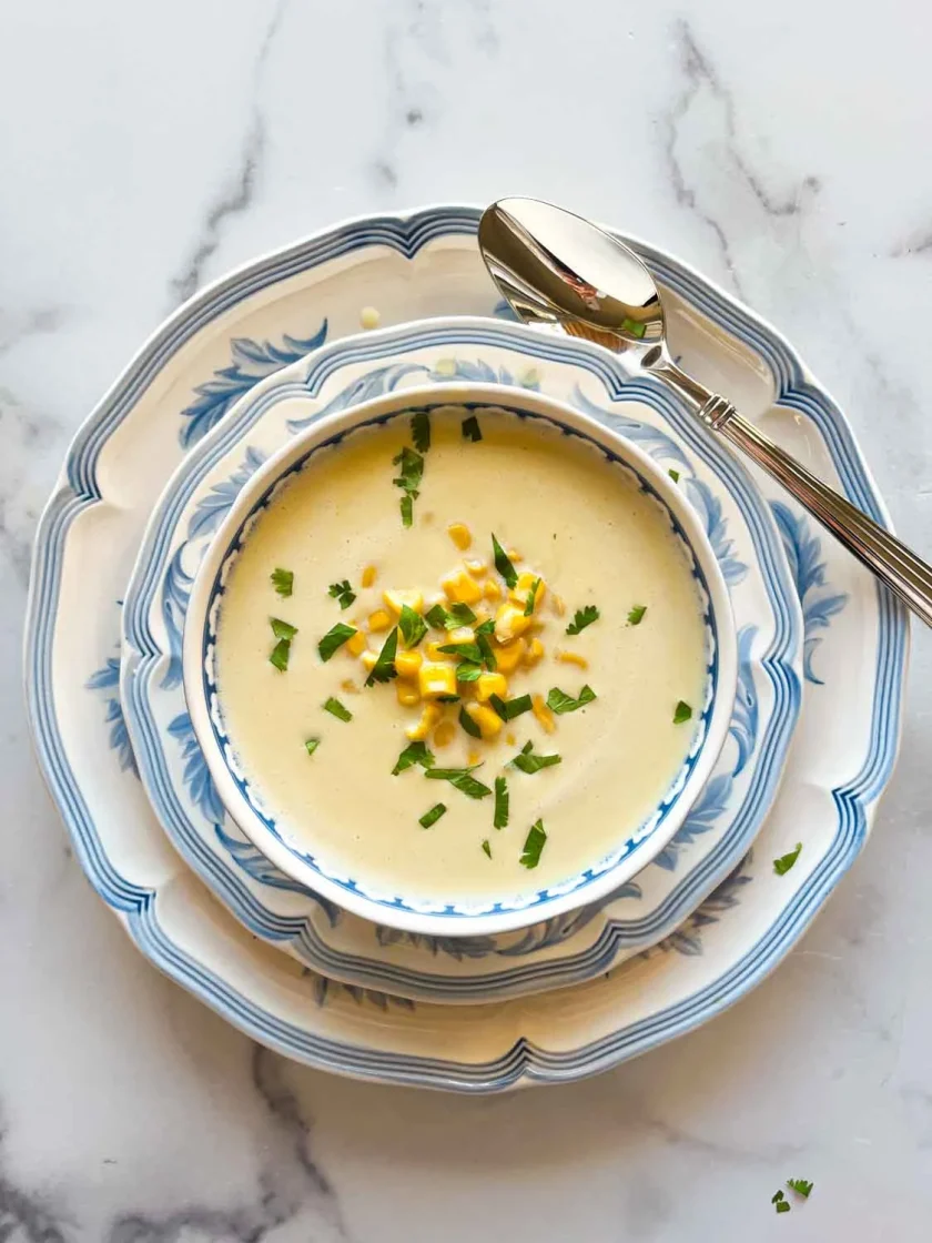 Un cuenco de sopa cremosa con maíz y hierbas en platos azules y blancos con una cuchara al lado.