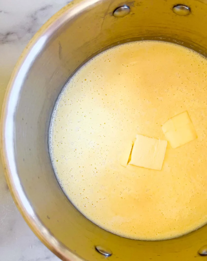 Una olla de cremosa mezcla amarilla con dos trozos de mantequilla flotando encima.