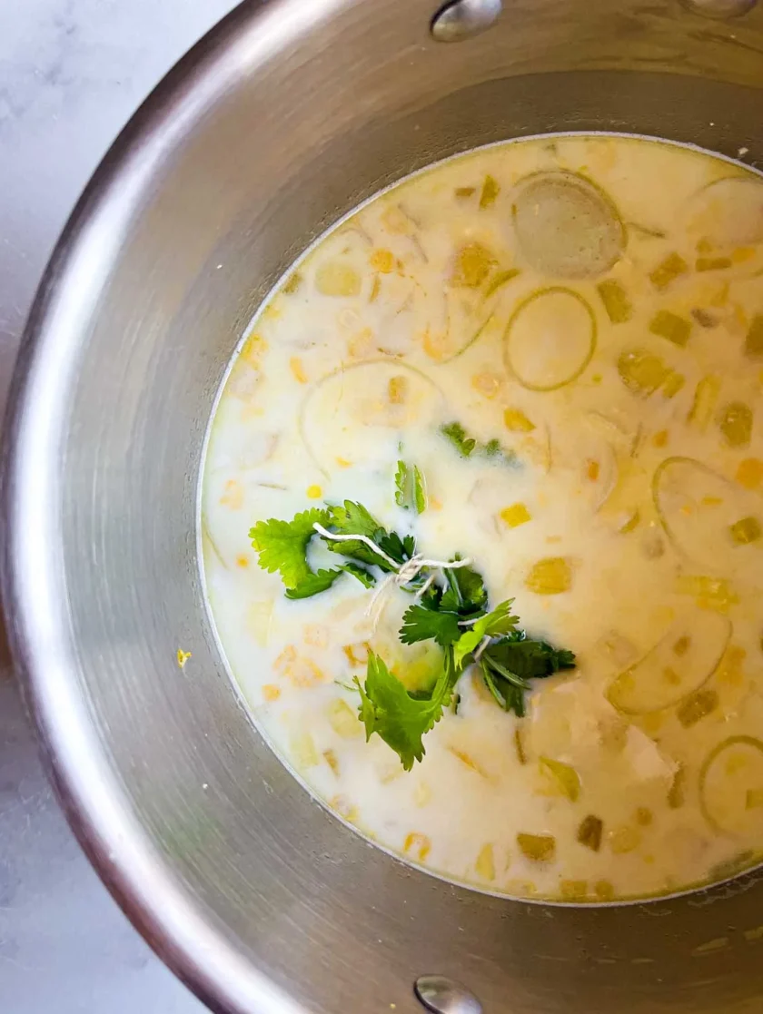 Una olla de sopa cremosa con maíz, puerros y un manojito de cilantro por encima.