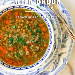 A bowl of lentil soup with bacon, garnished with herbs, on stacked blue and white plates with a spoon.