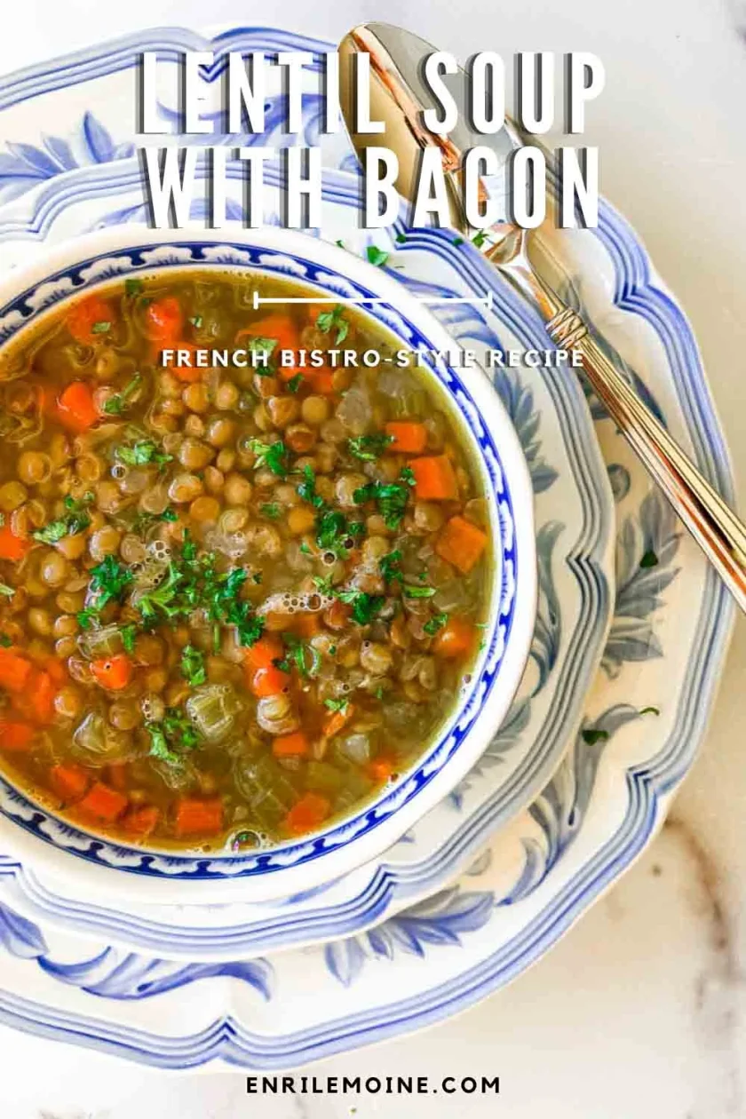 A bowl of lentil soup with bacon, garnished with herbs, on stacked blue and white plates with a spoon.
