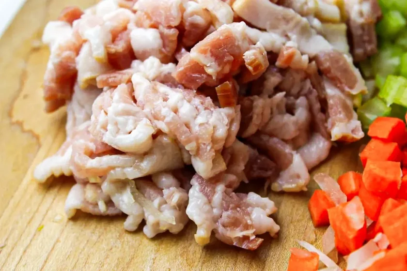 Chopped smoked bacon on a wooden board, with diced carrots and celery nearby.