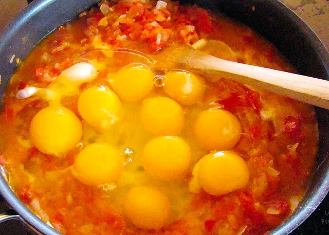 Los huevos se echan en una sartén con tomates y cebollas picados, removiéndolos con una cuchara de madera.