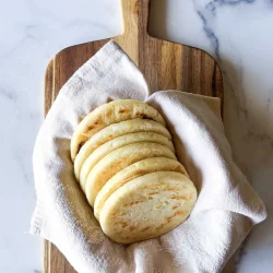 Telita arepas on a beige linen towel, over a wooden cutting board.