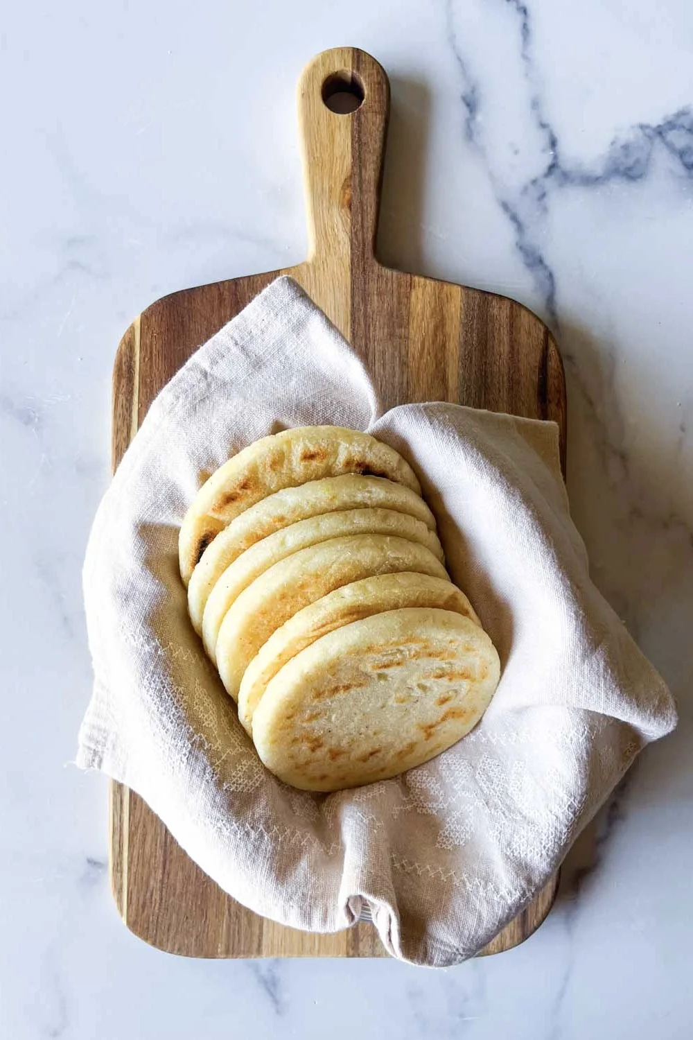 Arepas tipo telistas sobre una toalla de lino beige, en una tabla de madera sobre una superficie sde mármol.