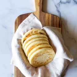 Arepas tipo telistas sobre una toalla de lino beige, en una tabla de madera sobre una superficie sde mármol.