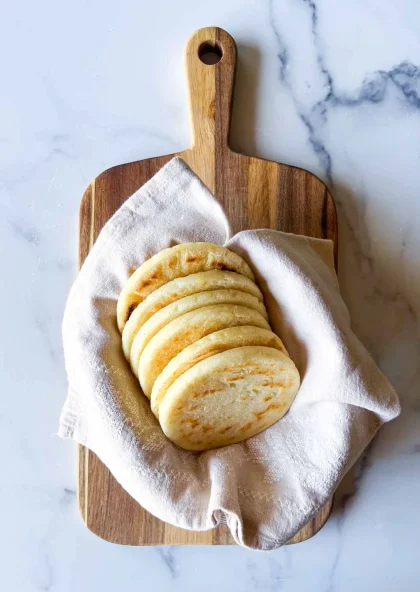 Arepas tipo telistas sobre una toalla de lino beige, en una tabla de madera sobre una superficie sde mármol.