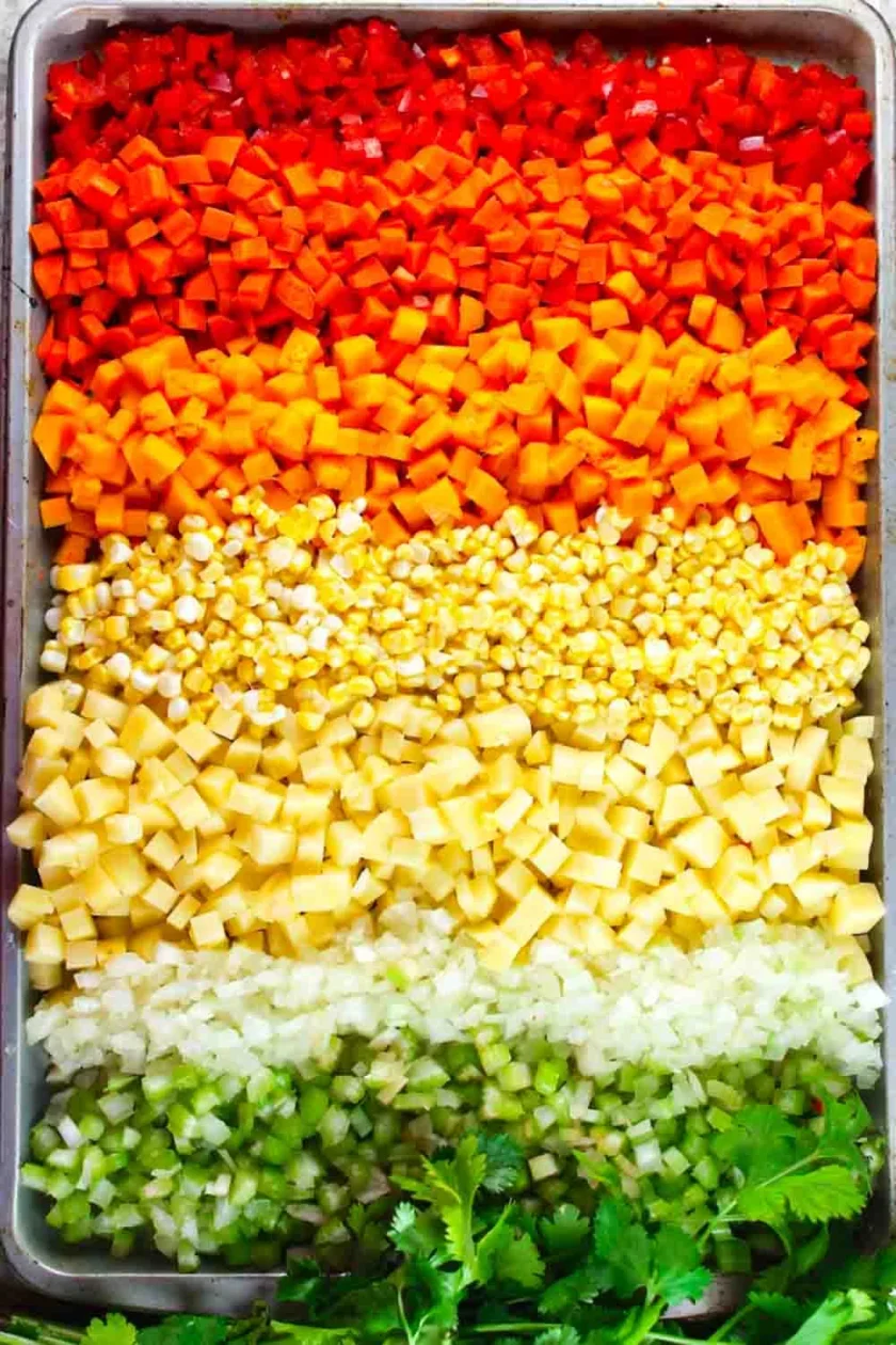 Verduras cortadas en dados y dispuestas en filas de colores: rojo, naranja, amarillo, blanco, verde, con un poco de cilantro en la parte inferior.