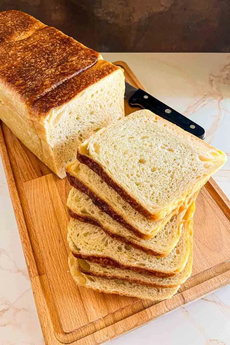 A loaf of sliced sourdough sandwich bread on a wooden cutting board with a knife next to it, perfect for your favorite sourdough sandwich bread recipe.