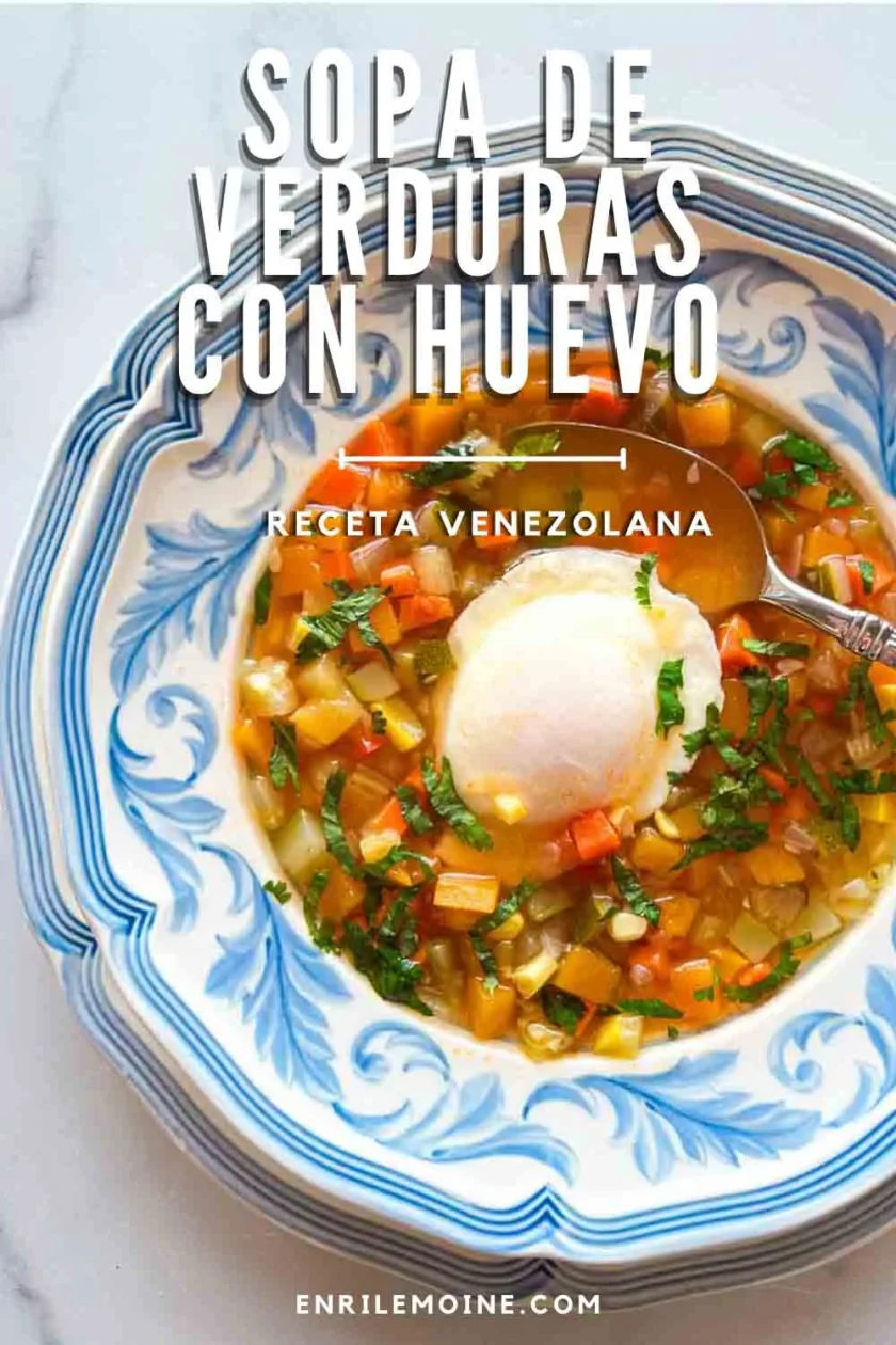 Tazón de sopa de verduras venezolana con un huevo escalfado, adornado con hierbas, en un plato azul y blanco.