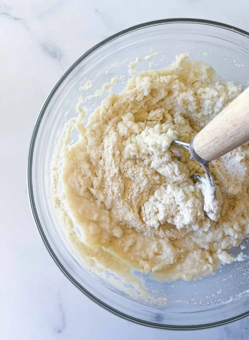 Masa de arepas en un tazón de vidrio con una batidor danés adentro.
