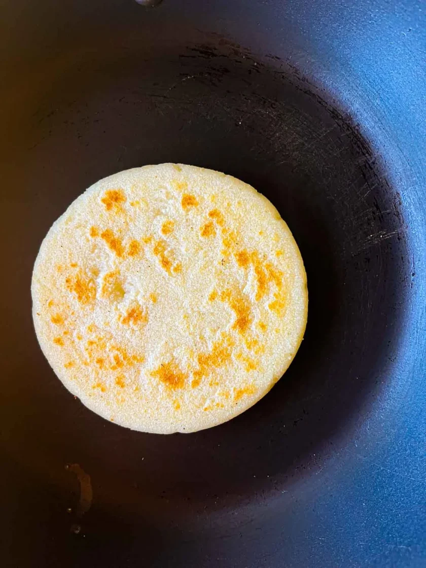 Una arepa asada en un sarten negro.
