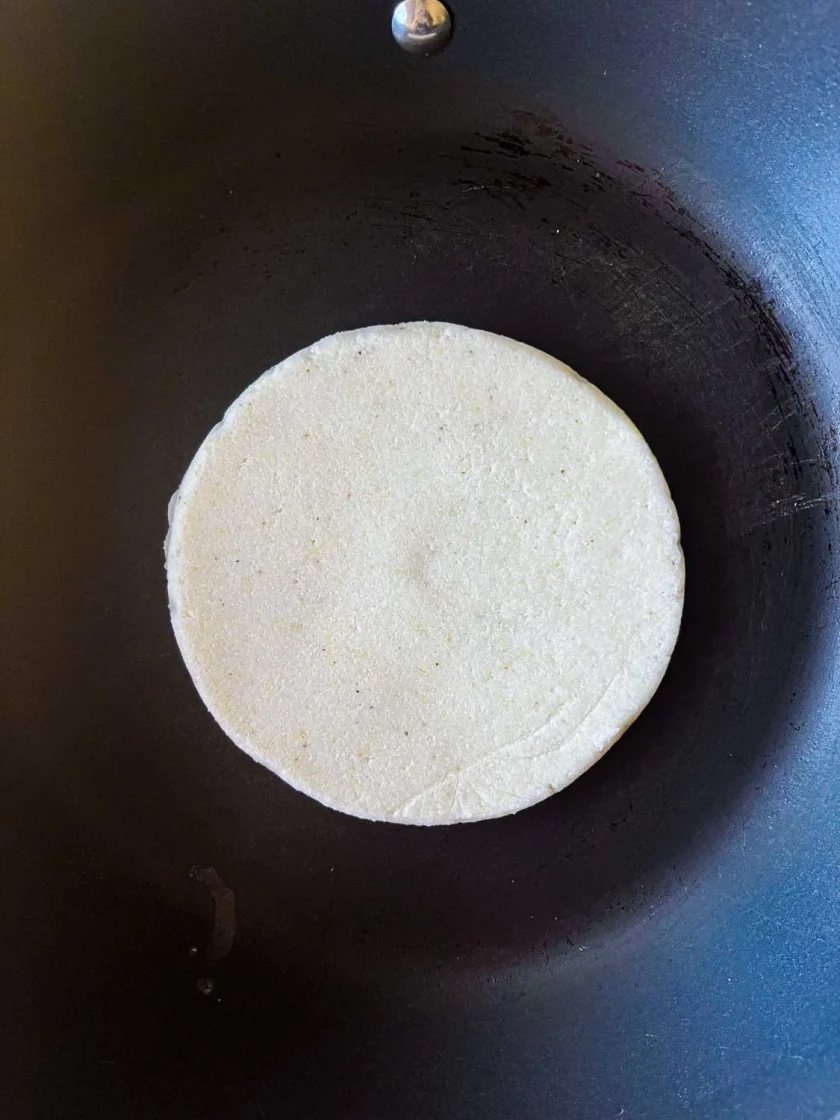 una arepa cruda en un sarten negro.