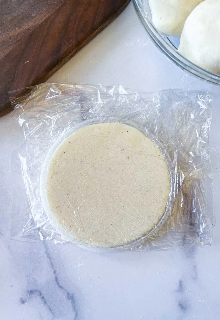 una arepa formada dentro de una tapa plásticacubierta con film plástico, sobre una superficie de mármol.