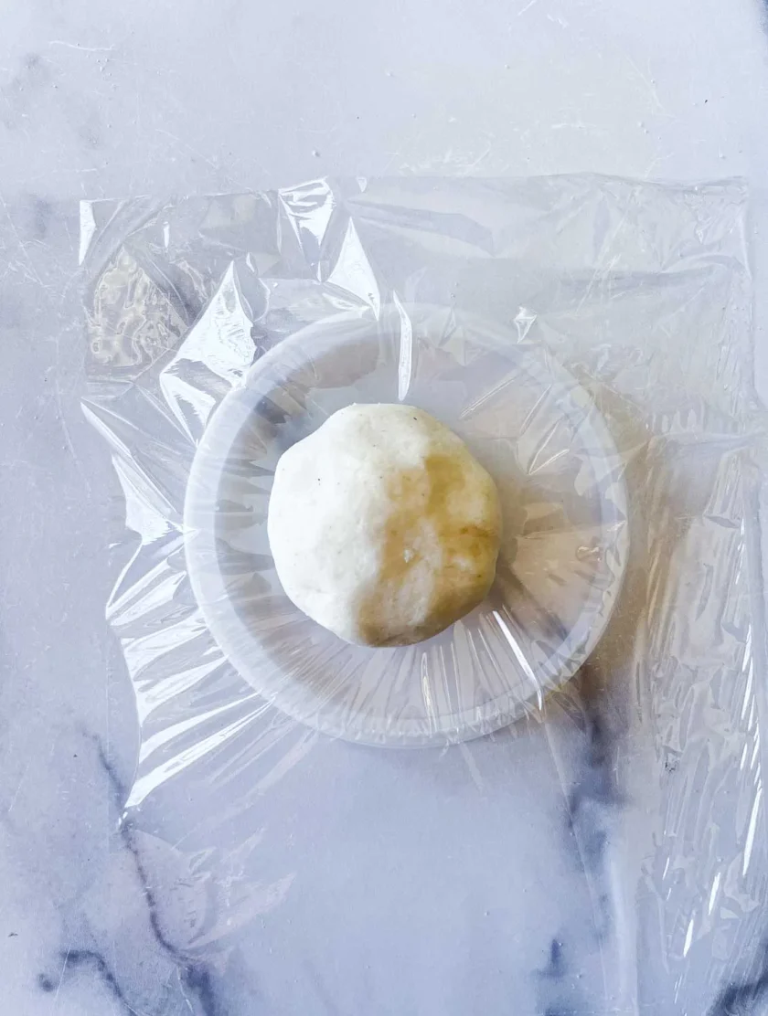 una bolita de masa de arepa sobre una tapa plástica. La tapa esta cubierto con film plástico.