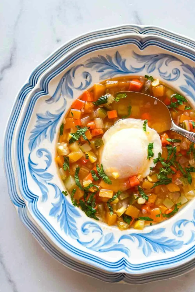 Venezuelan Veggie Soup with Egg and Cilantro served in a blue and white bowl, featuring a poached egg and fresh herbs on a marble surface.