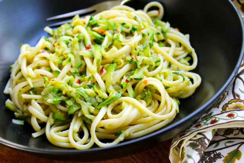 Un plato negro con linguini con salsa de calabacín y anchoas.