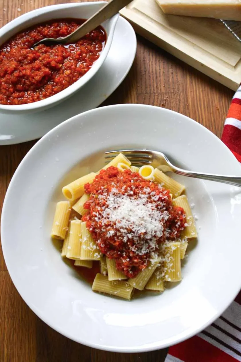 A bowl of rigatoni dressed with fake Bolognese sauce and Parmesan cheese, on a wooden surface.