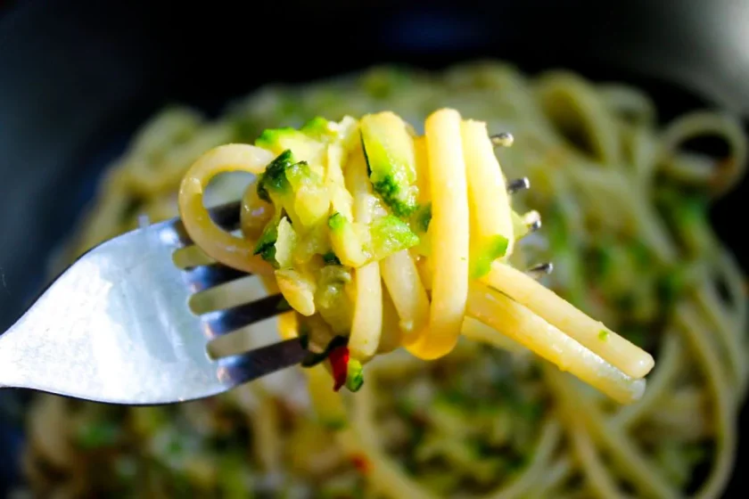 Un tenedor con un bocado de linguini con calabacín y anchoas.