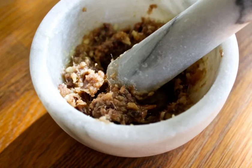 Un mortero de mármol con anchoas desmenuzadas, sobre una superficie de madera.
