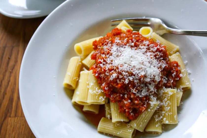Close up of a white pasta bowl with rigatoni dressed with fake Bolognese sauce and grated Parmesan cheese.