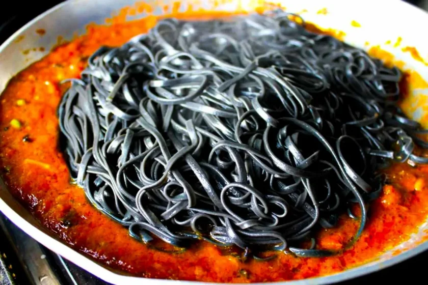 Linguini negro en un sartén con salsa de tomate alla puttanesca.