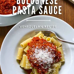 A bowl of rigatoni dressed with fake Bolognese sauce and Parmesan cheese, on a wooden surface.